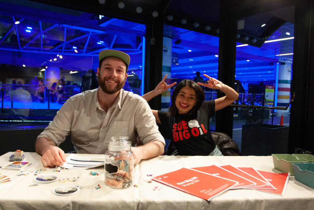 Two young people posing at a welcome table at the Sue Big Oil launch party