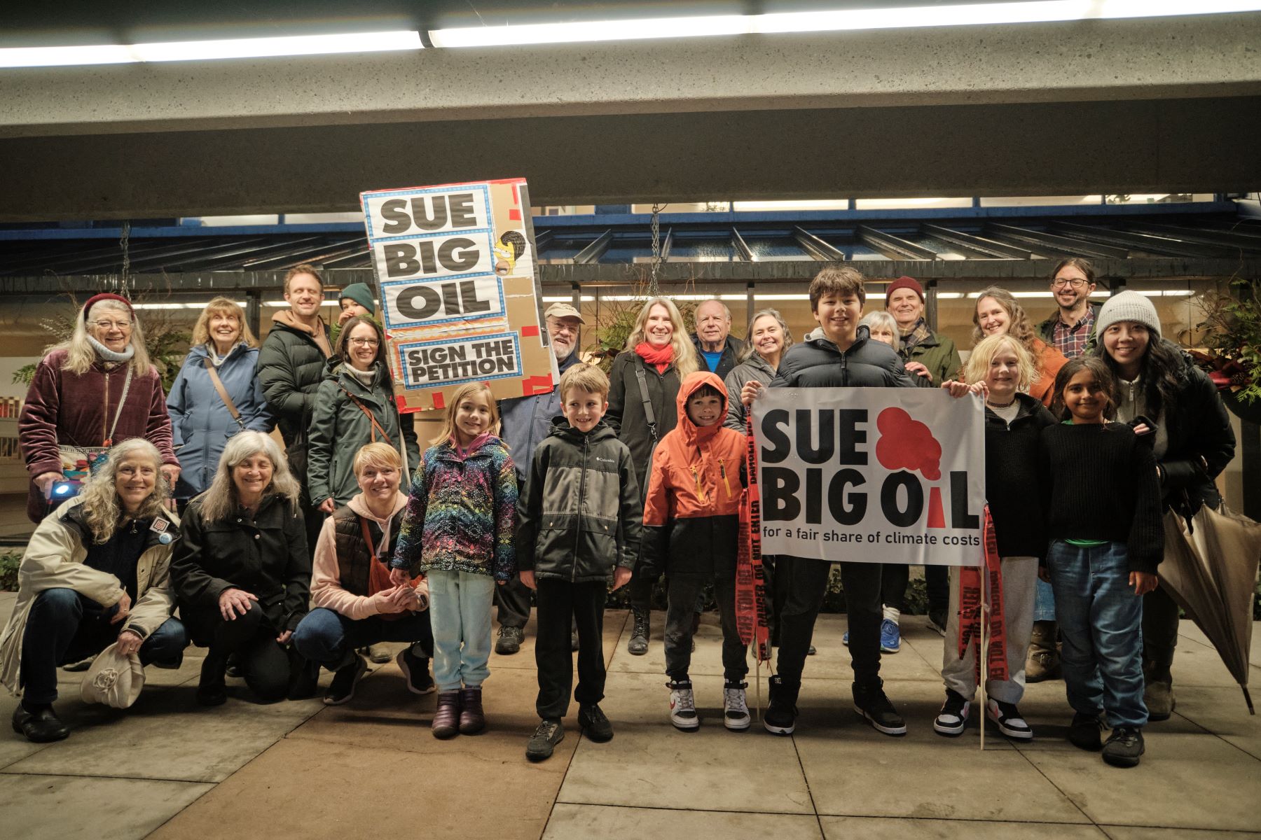 Diverse group of people and kids with Sue Big Oil signs