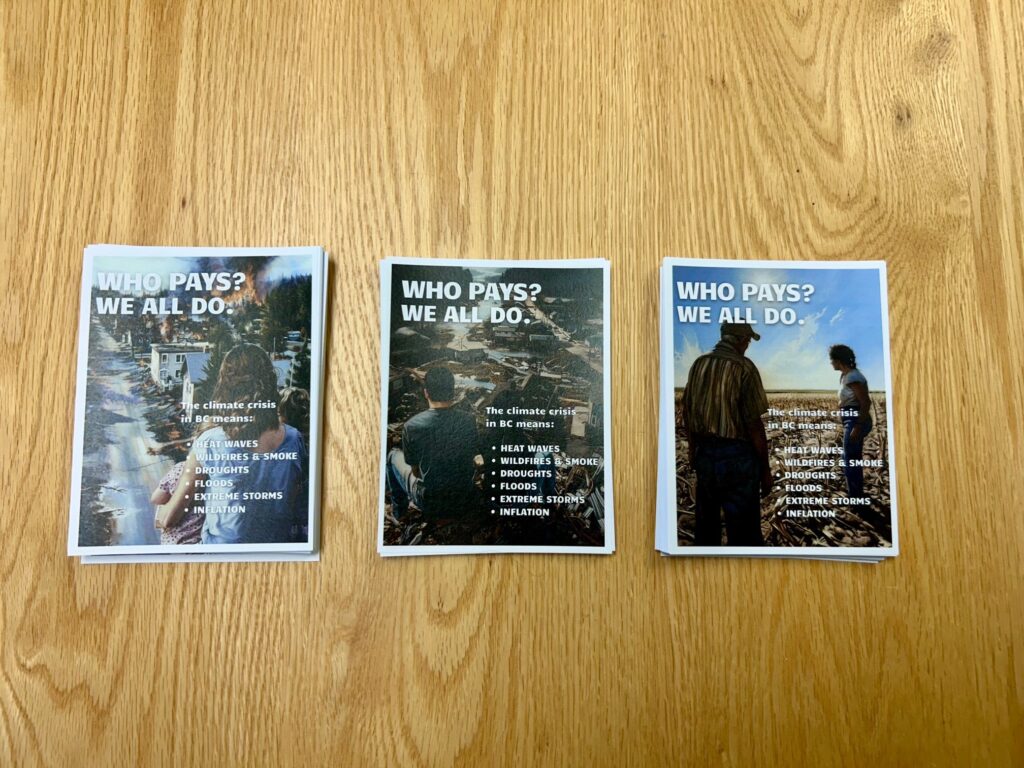 Three stacks of flyers on a wooden table, with images depicting climate impacts and message saying "Who Pays? We all do"