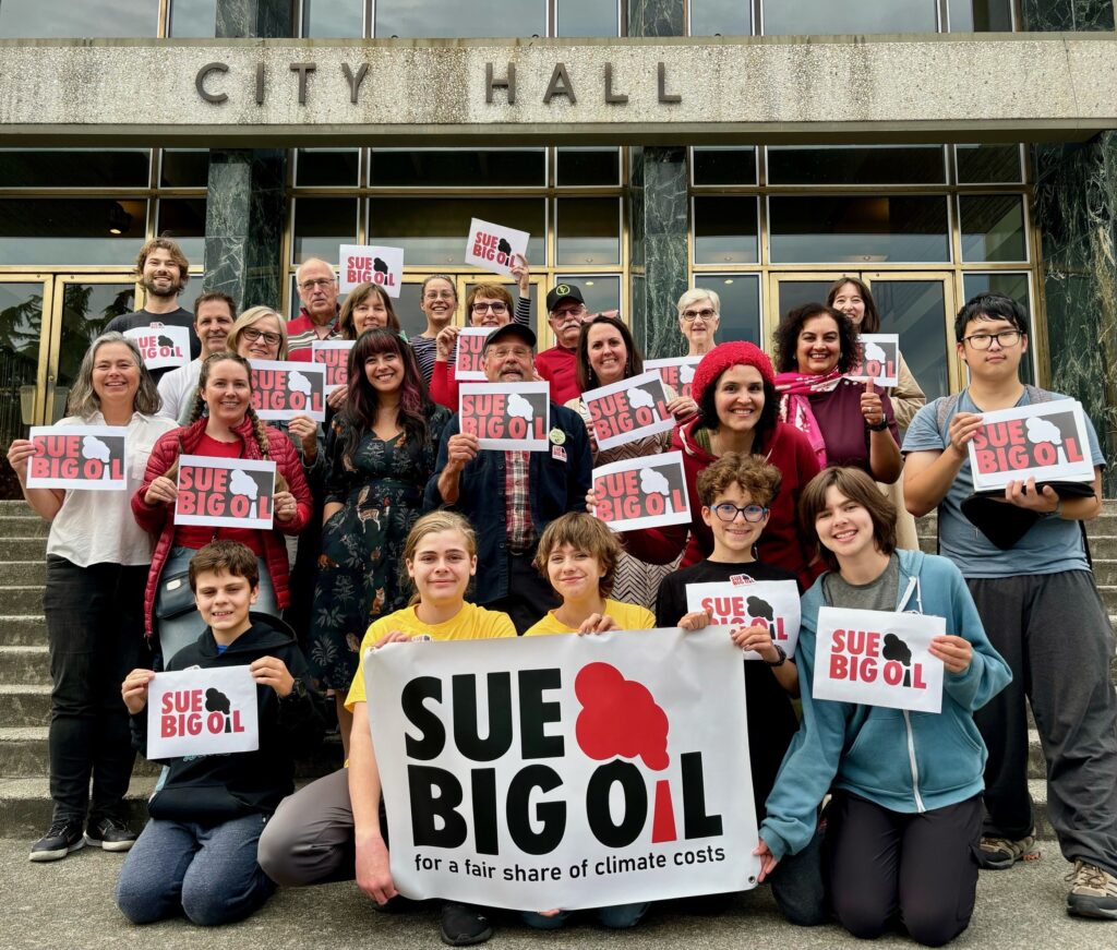 A group of approx. 20 people holding Sue Big Oil signs on steps at New Westminster City Hall